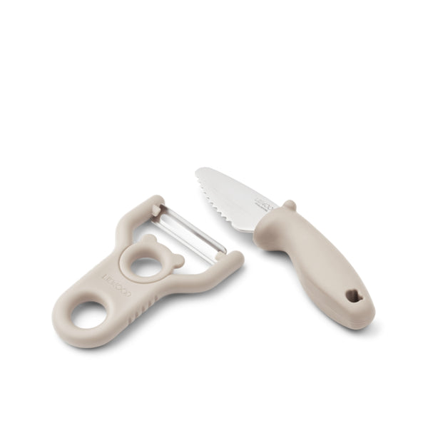 Conjunto infantil de descascador e faca com lâminas em aço inoxidável e pegas adaptadas às crianças para preparação de alimentos.