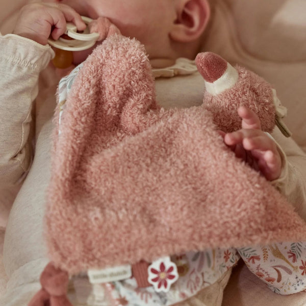 Doudou Flamingo em tecido macio com etiquetas sensoriais e fita para prender chupeta ou mordedor, ideal para confortar e estimular o bebé desde os primeiros meses.